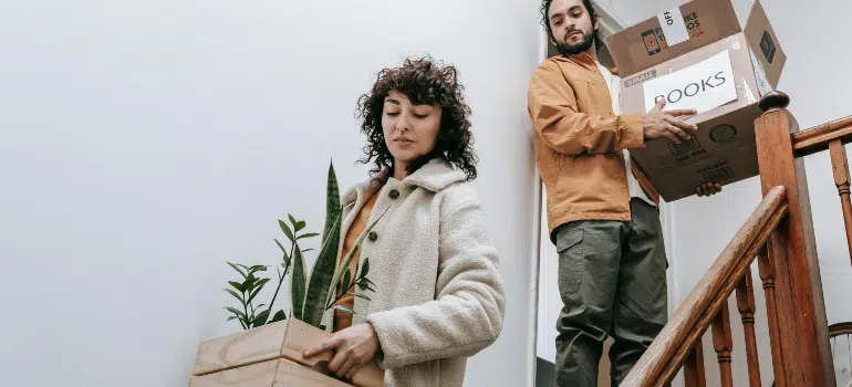 Cincinnati Apartment vs House Moves: What’s the Difference? 2 Man and woman carefully carrying moving boxes and plants down a staircase during a home relocation.